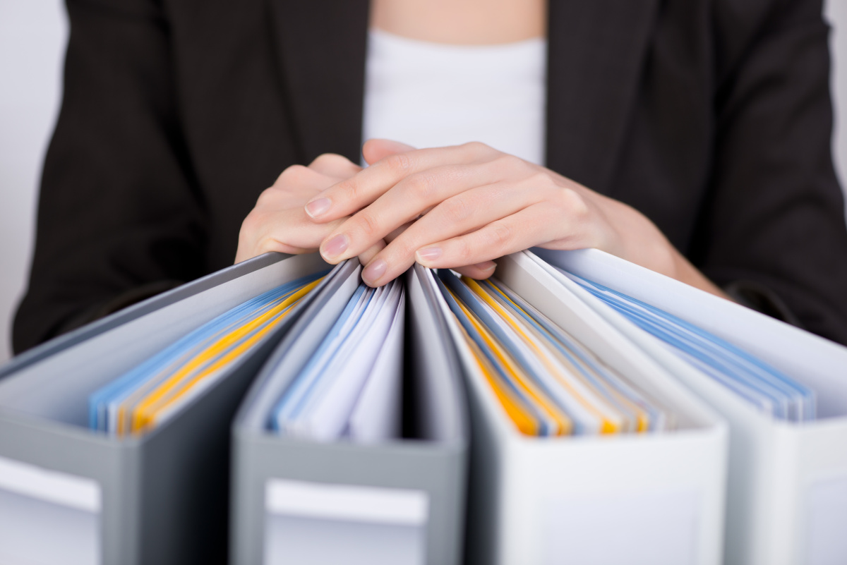 A women in a suit resting her hands on multiple binders, that are full of paper work