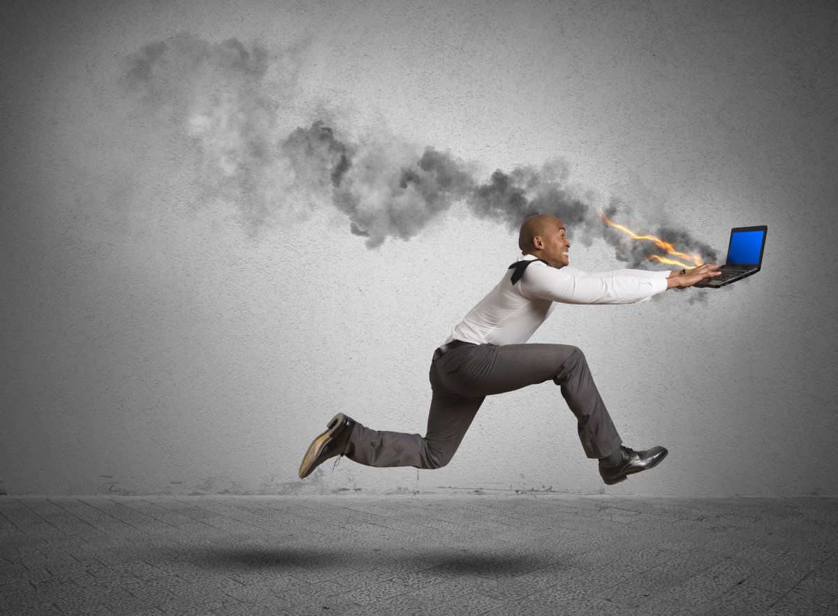 Man in business attire running while typing on a flaming laptop.