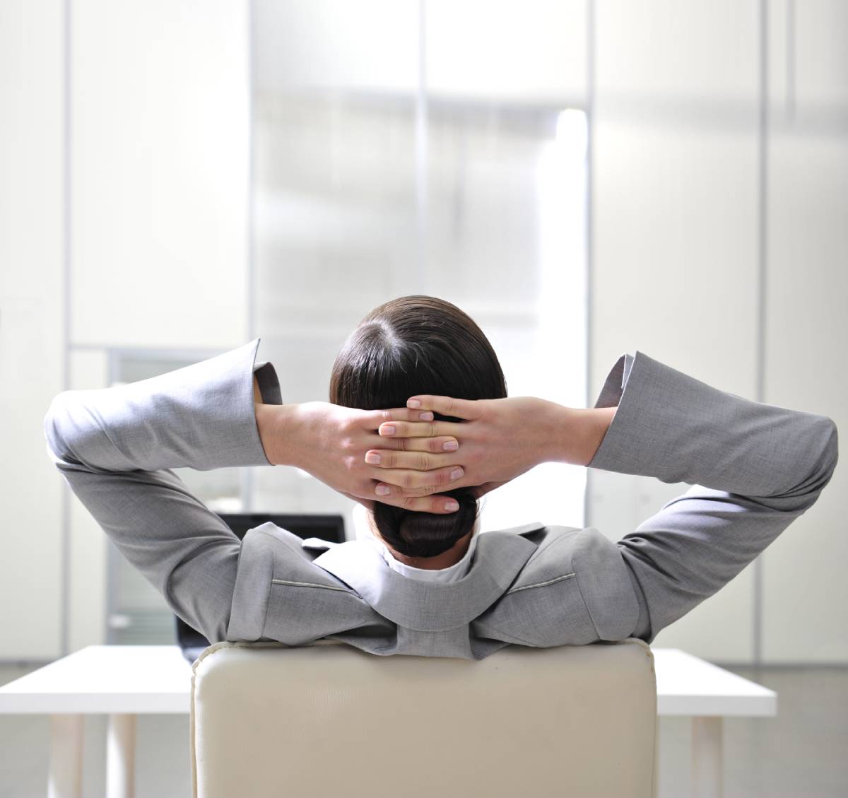 Back of a Man in business attire, leaning back in a chair with hands behind his head 