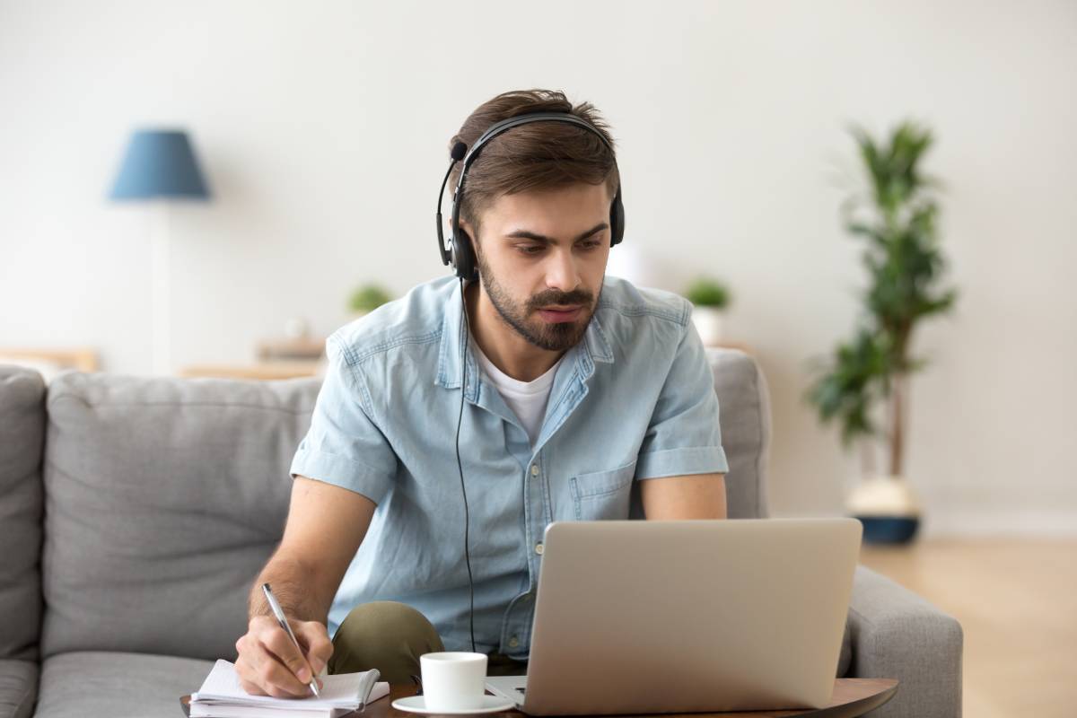 A bearded man working from home using a headset and a laptop