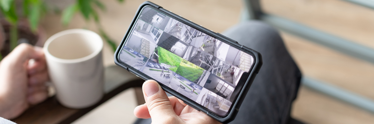 Close up of a a phone showing multiple security camera feeds, being viewed by someone relaxing at home with a mug in the other hand.