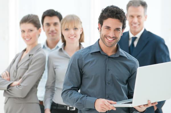 Smiling businessman holding laptop with blurred colleagues in background